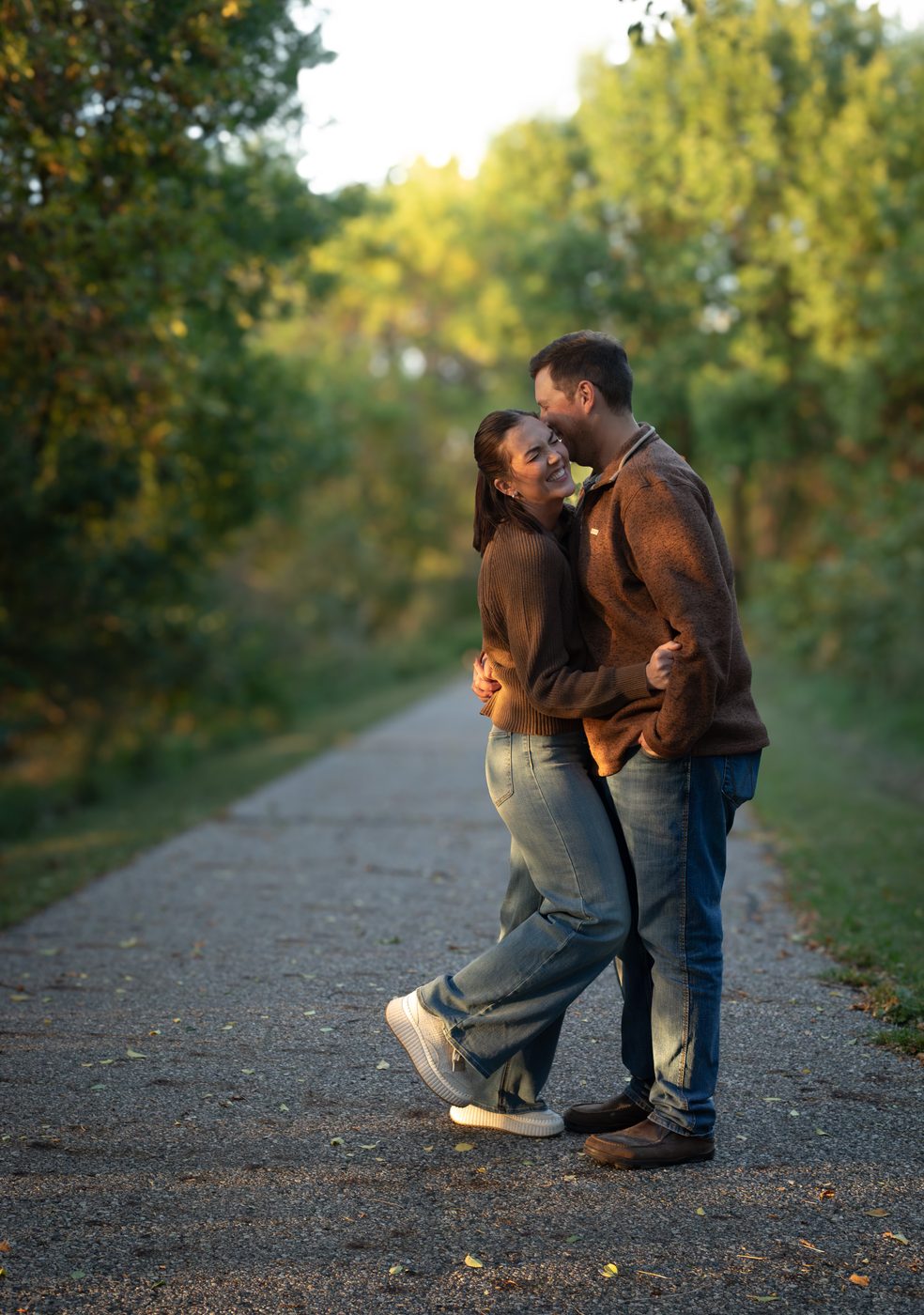 Couple kissing on a tree lined path during an engagement session