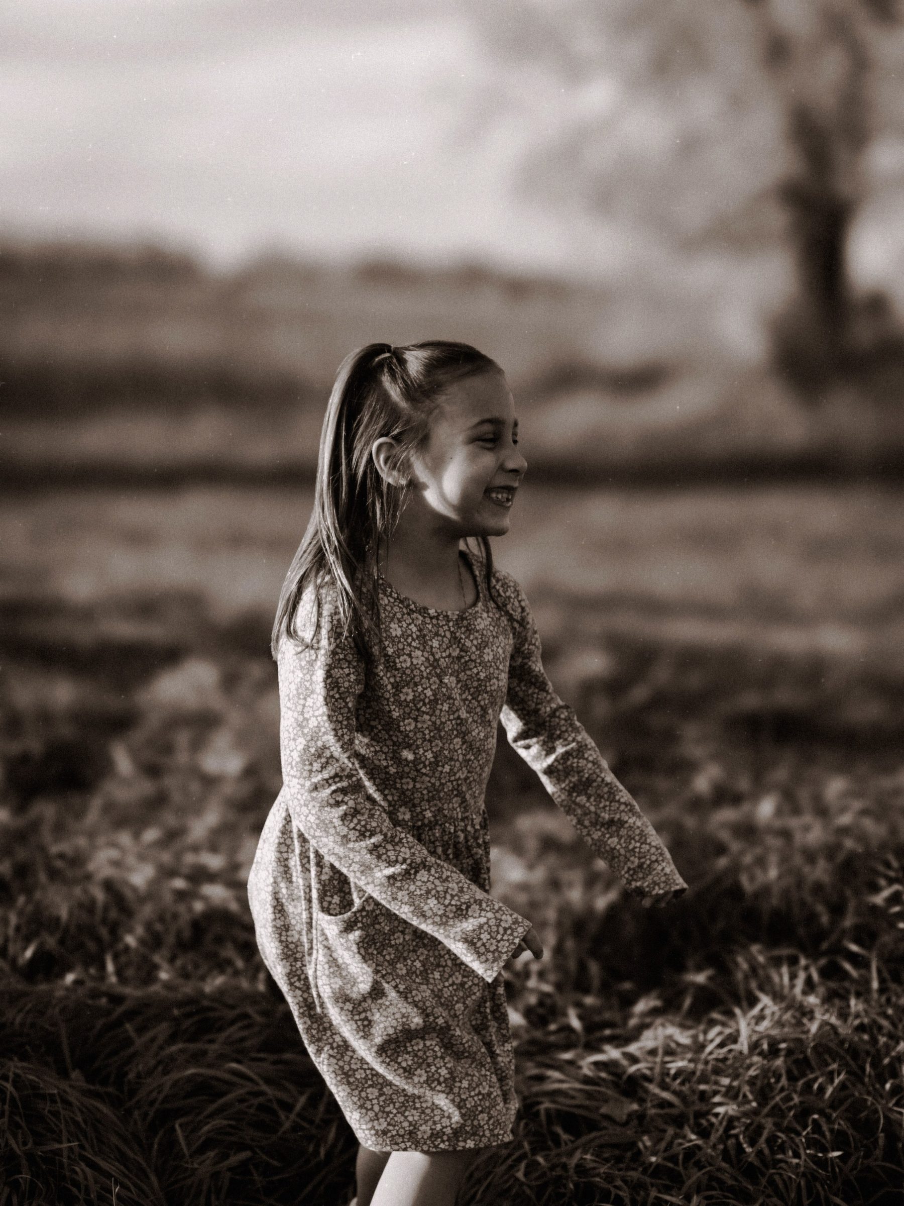 Young girl dancing through tall grass in black and white