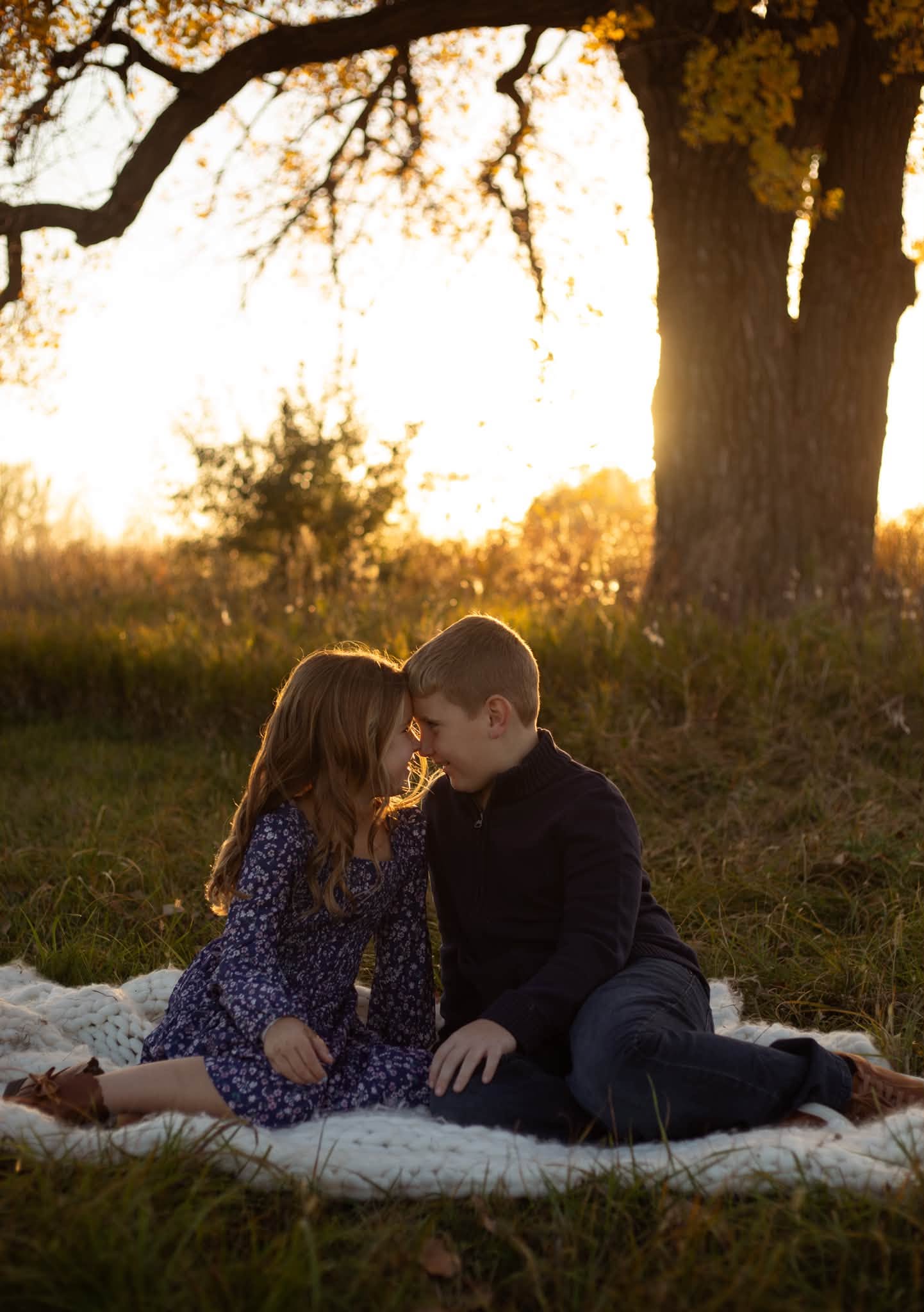 Brother and sister sharing a quiet moment under an oak tree at sunset